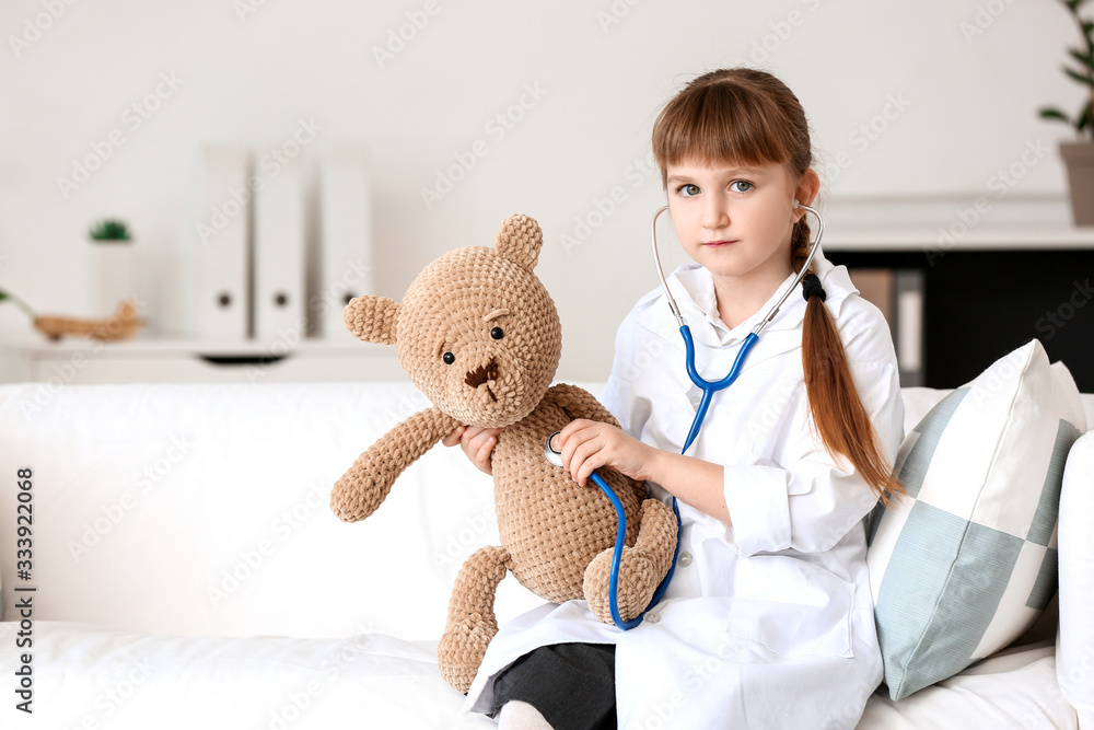 Cute little doctor playing with teddy bear in clinic