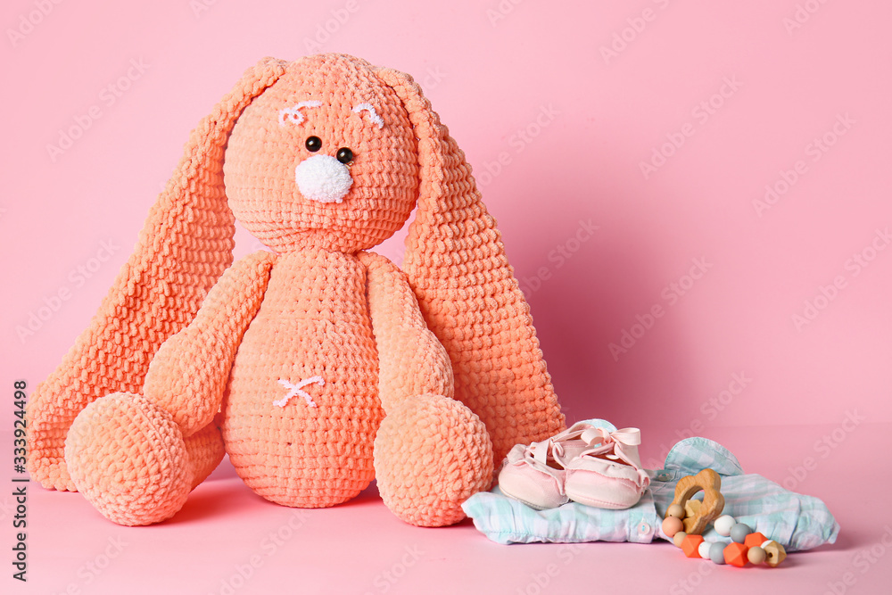 Cuddly bunny with baby clothes on color background