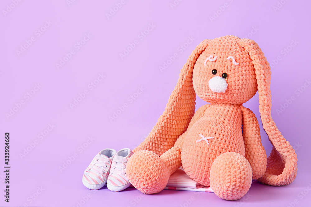 Cuddly bunny with baby clothes on color background