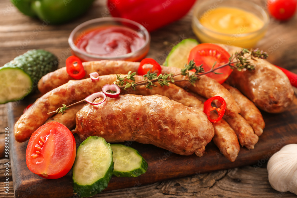 Board with tasty grilled sausages and vegetables on table