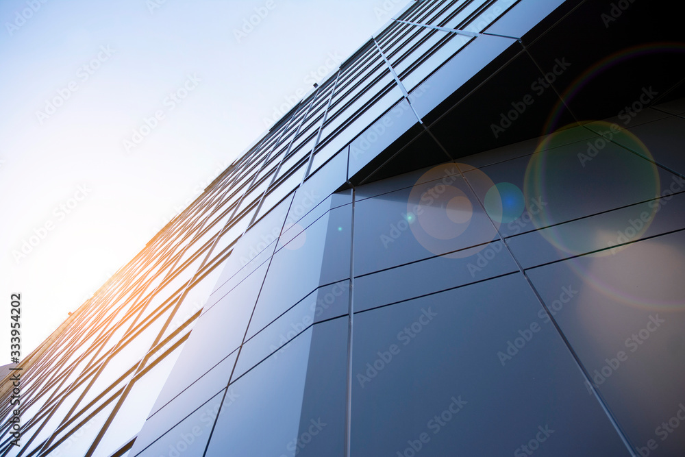 Facade of modern glass building at sunset. Warm and cool tone contrast. Sun flare.