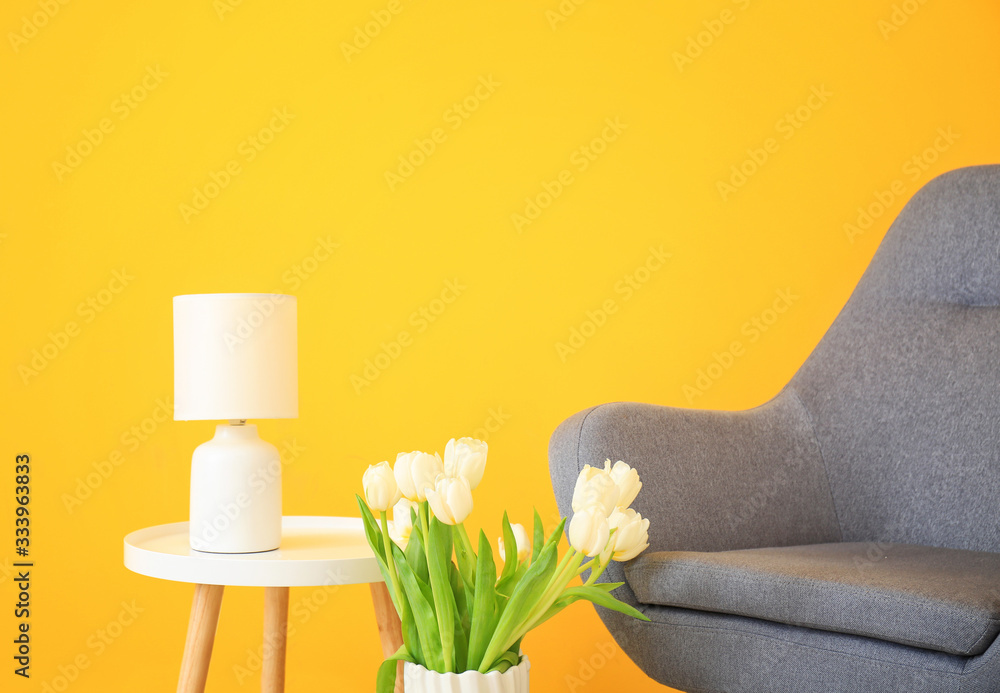 Armchair, bouquet of flowers and table near color wall