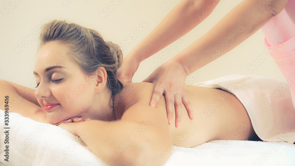 Relaxed woman getting back massage in luxury spa with professional massage therapist. Wellness, heal