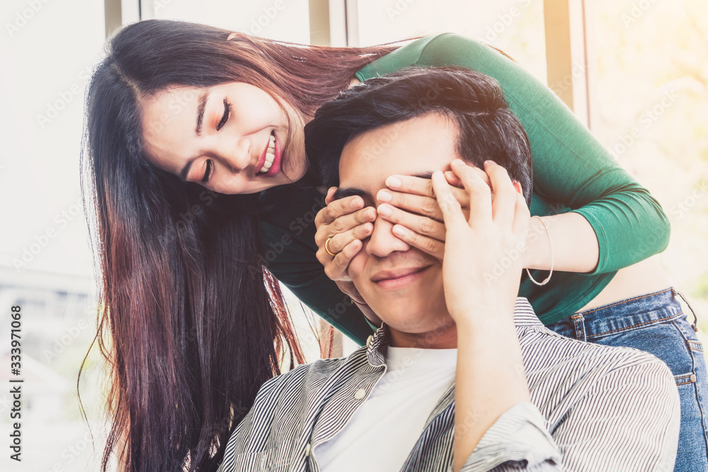 Happy Asian couple play covering eyes in living room.