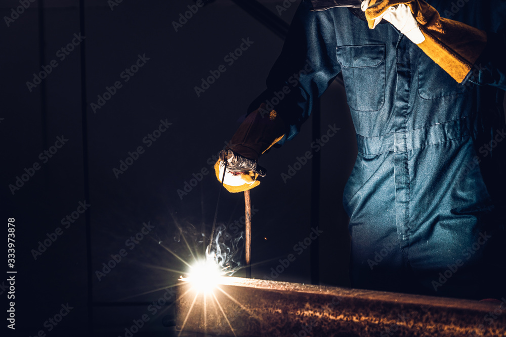 Metal welder working with arc welding machine to weld steel at factory while wearing safety equipmen