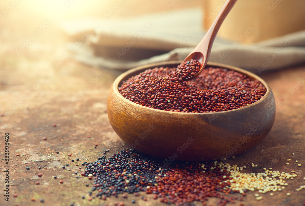 Red quinoa grains in a wooden spoon. Healthy food in a bowl. Seeds of white, red and black quinoa - 