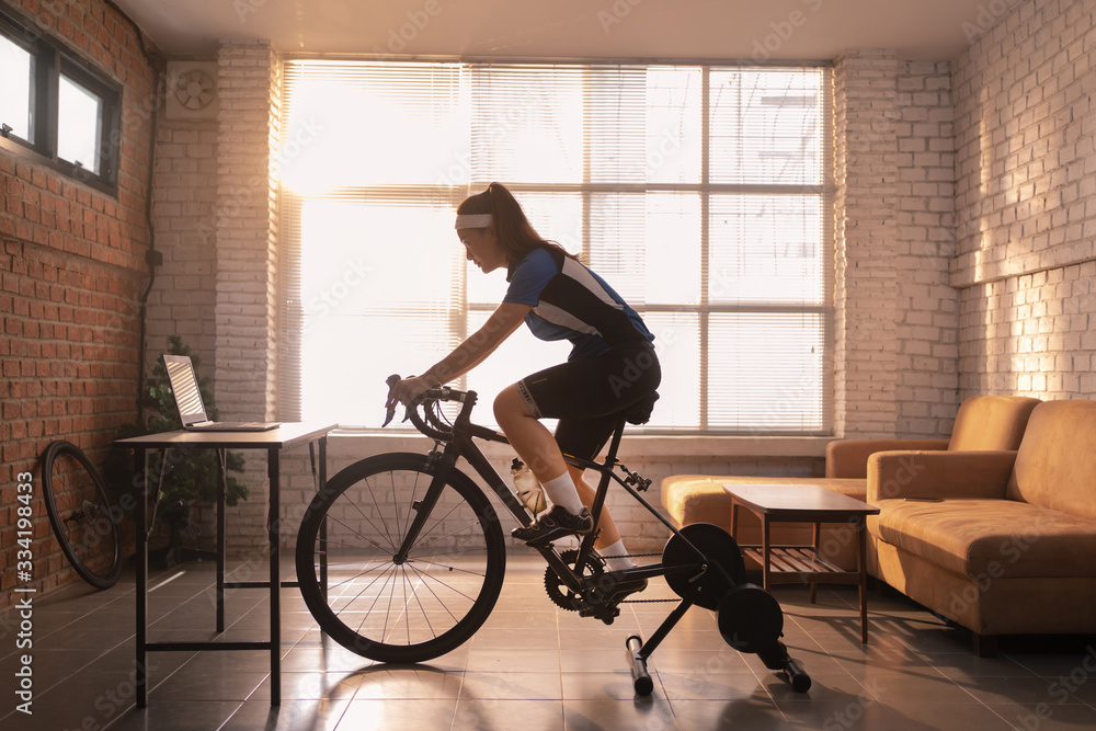 Asian woman cyclist. She is exercising in the house.By cycling on the trainer and play online bike g