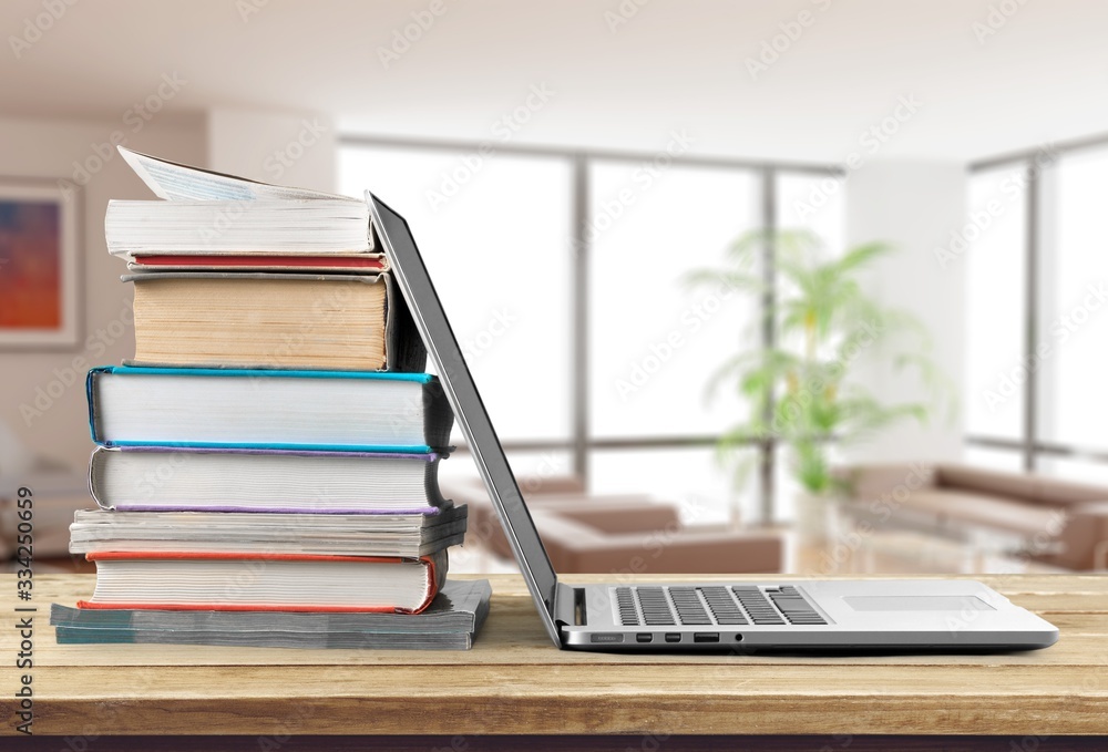 Stack of books with laptop on wooden table