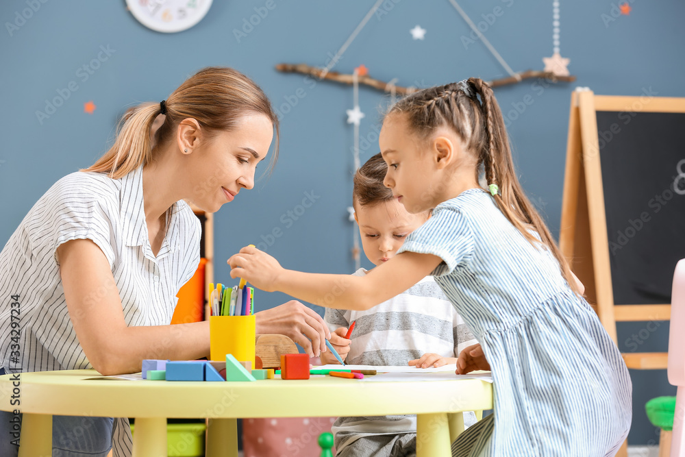 Nanny with cute little children playing and drawing at home