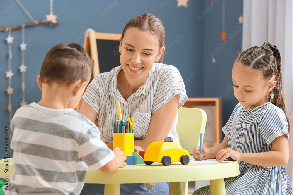 Nanny with cute little children playing and drawing at home