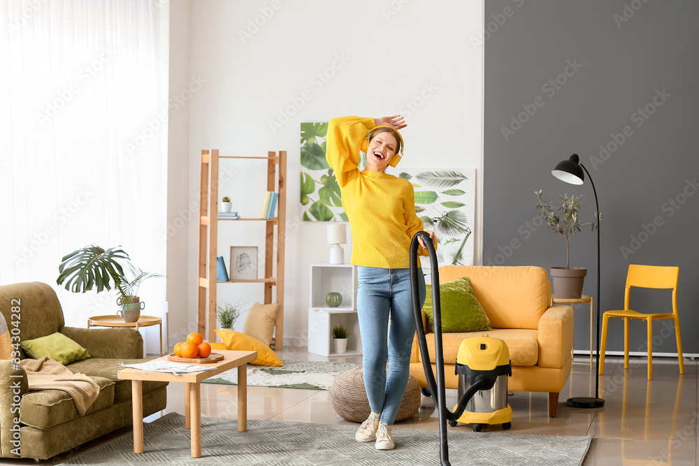 Young woman listening to music while hoovering floor at home