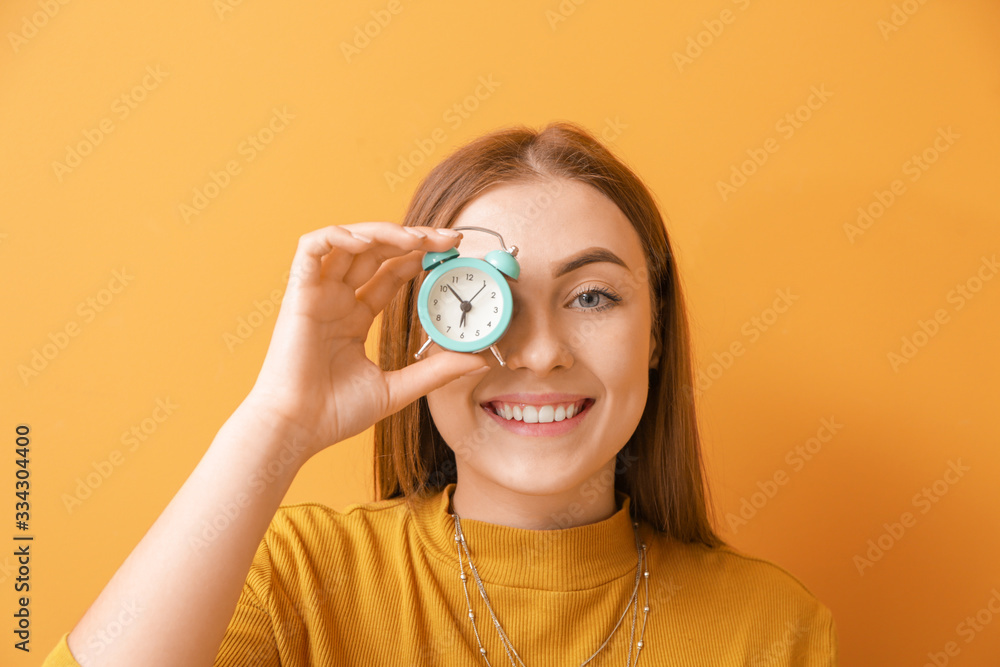 Beautiful young woman with alarm clock on color background