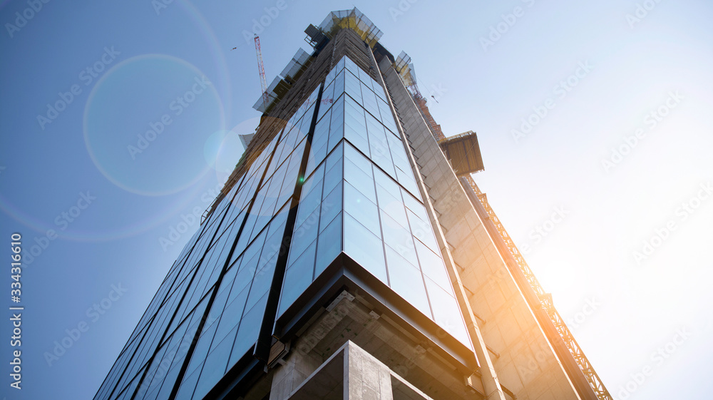 Building under construction and cranes under a cloudy sky. Modern architecture with sun ray. Constru