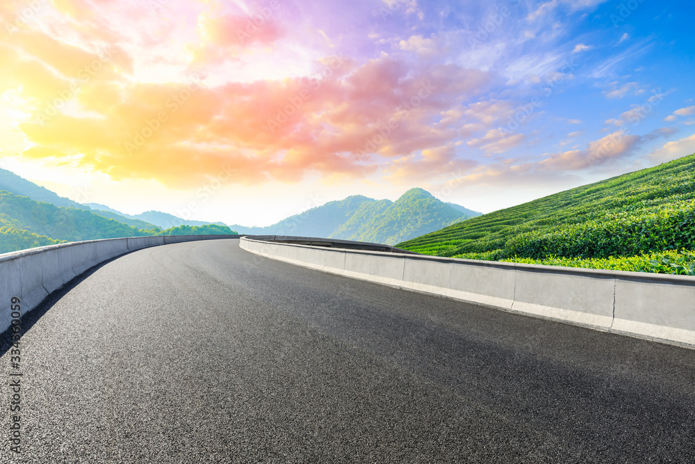 Empty asphalt road and green tea plantation nature landscape at sunset.