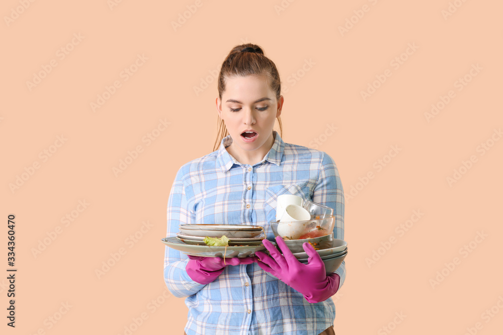 Shocked woman with dirty dishes on color background