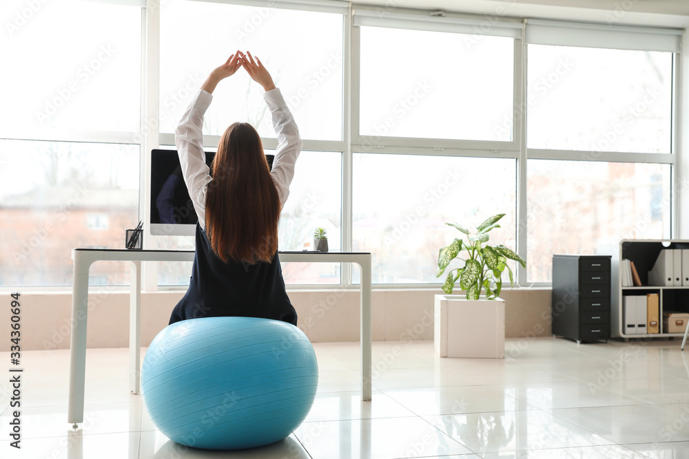 Businesswoman sitting on fitness ball while working in office