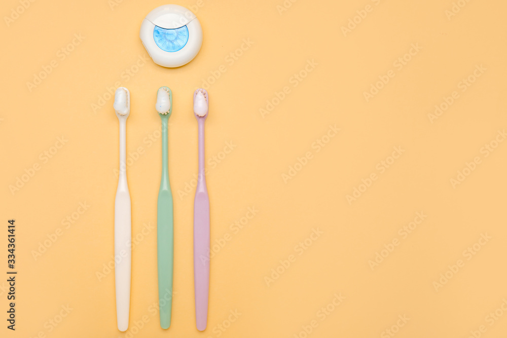 Tooth brushes with paste and dental floss on color background