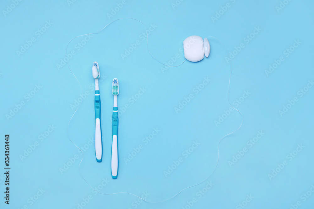 Tooth brushes with paste and dental floss on color background