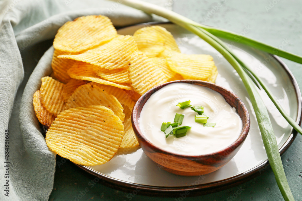 Tasty sour cream, green onion and potato chips on table