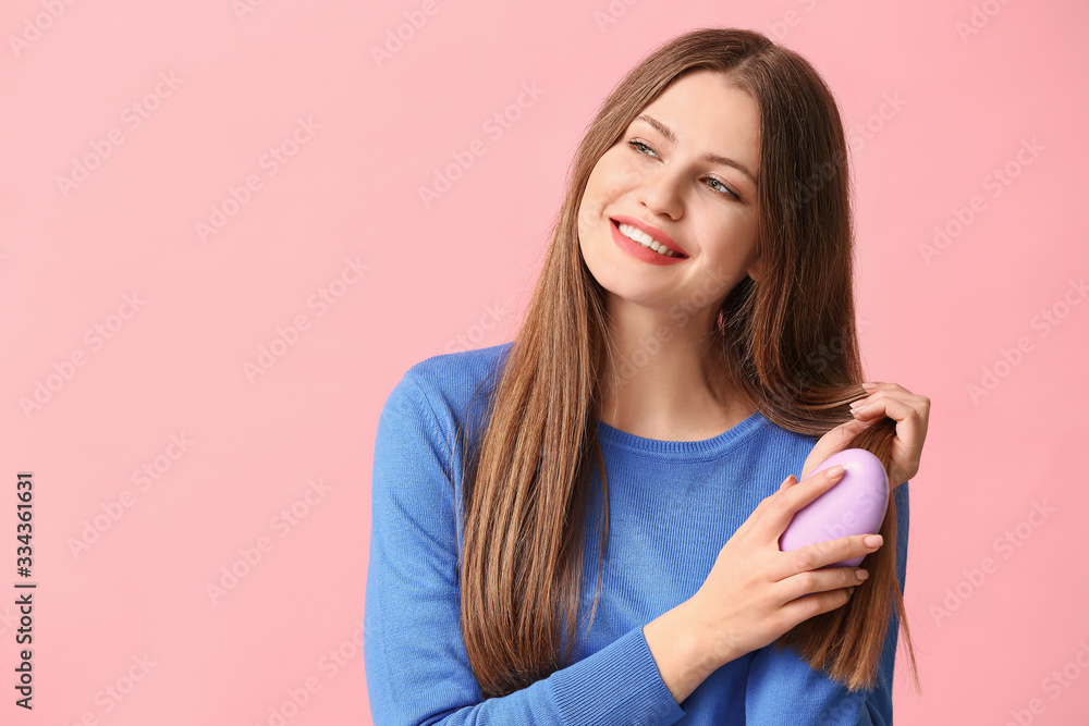 Beautiful young woman brushing hair on color background