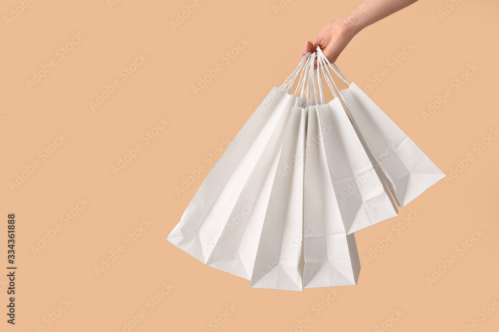 Female hand with paper shopping bags on color background