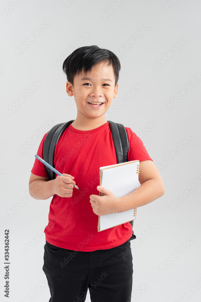 School boy with backpack writting something on his notebook, isolated on white.