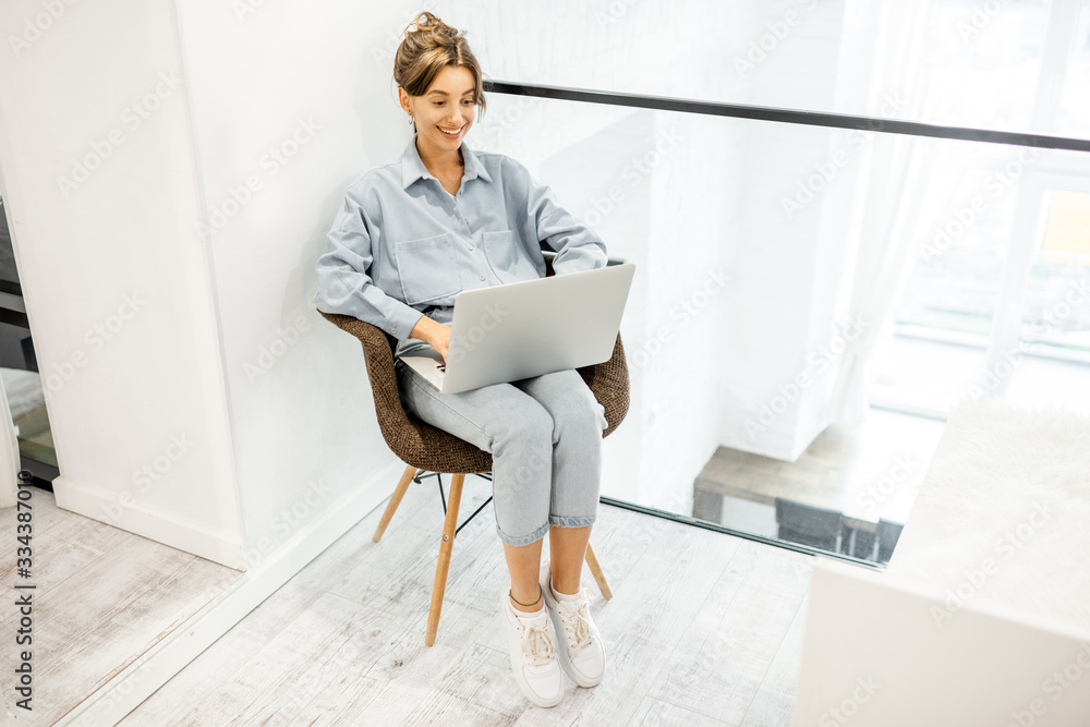 Young woman working on laptop while sitting on the comfortable chair at home. Work online from home 