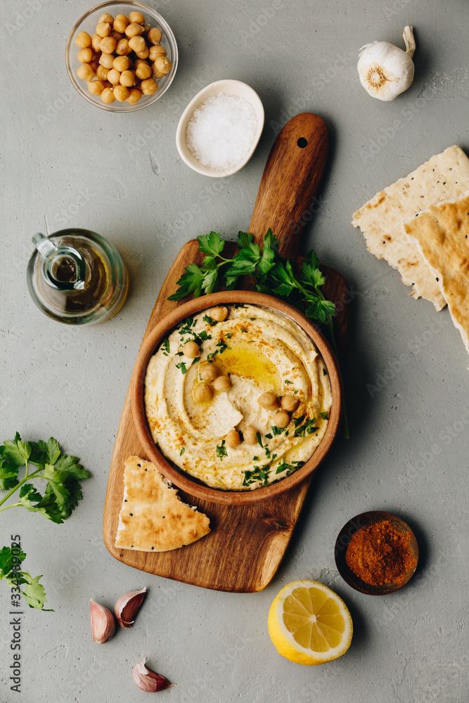 Large bowl of homemade hummus garnished with chickpeas, red sweet pepper, parsley and olive oil