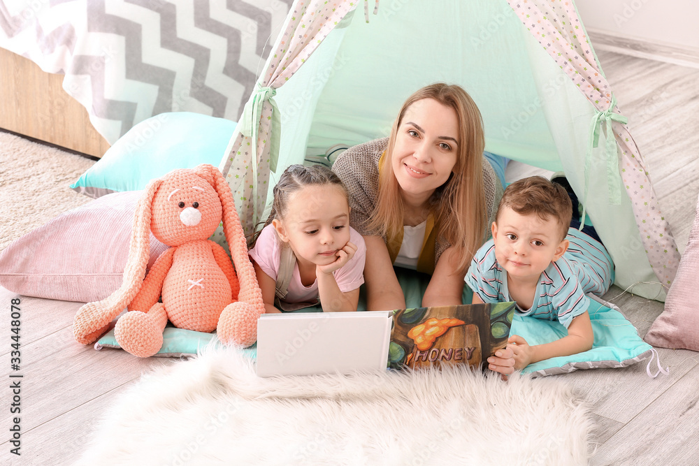 Nanny and cute little children reading book at home