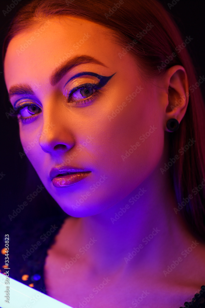 Toned portrait of beautiful woman with neon lamp on dark background