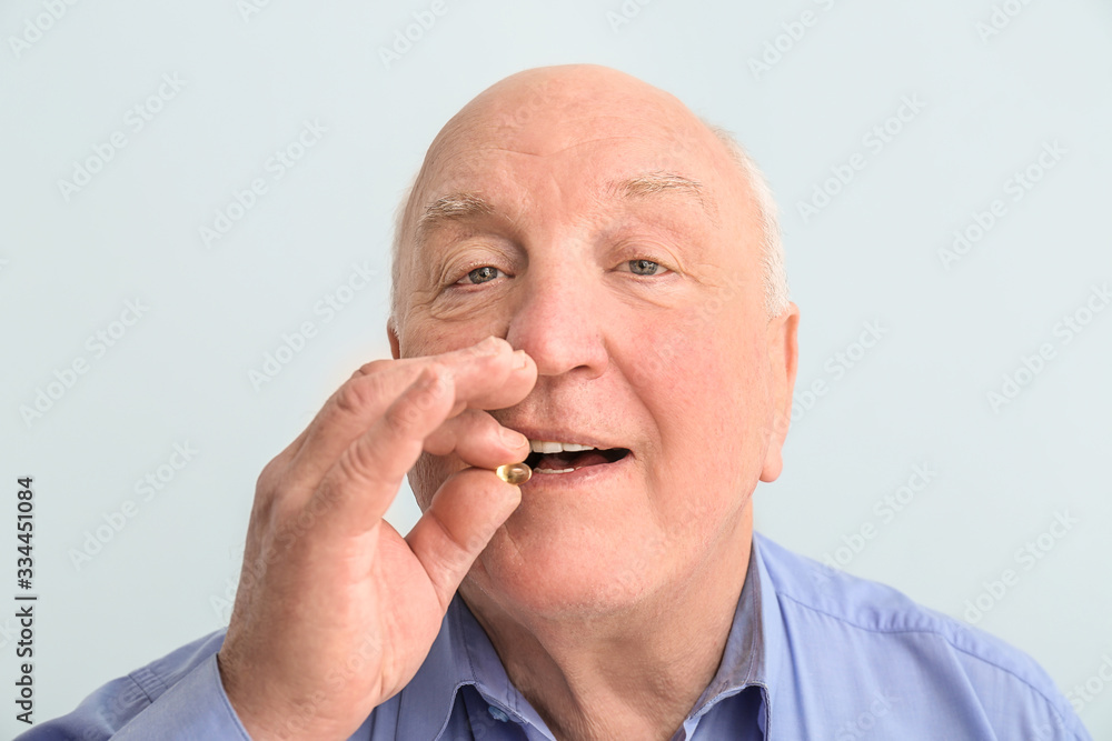 Senior man with fish oil on color background