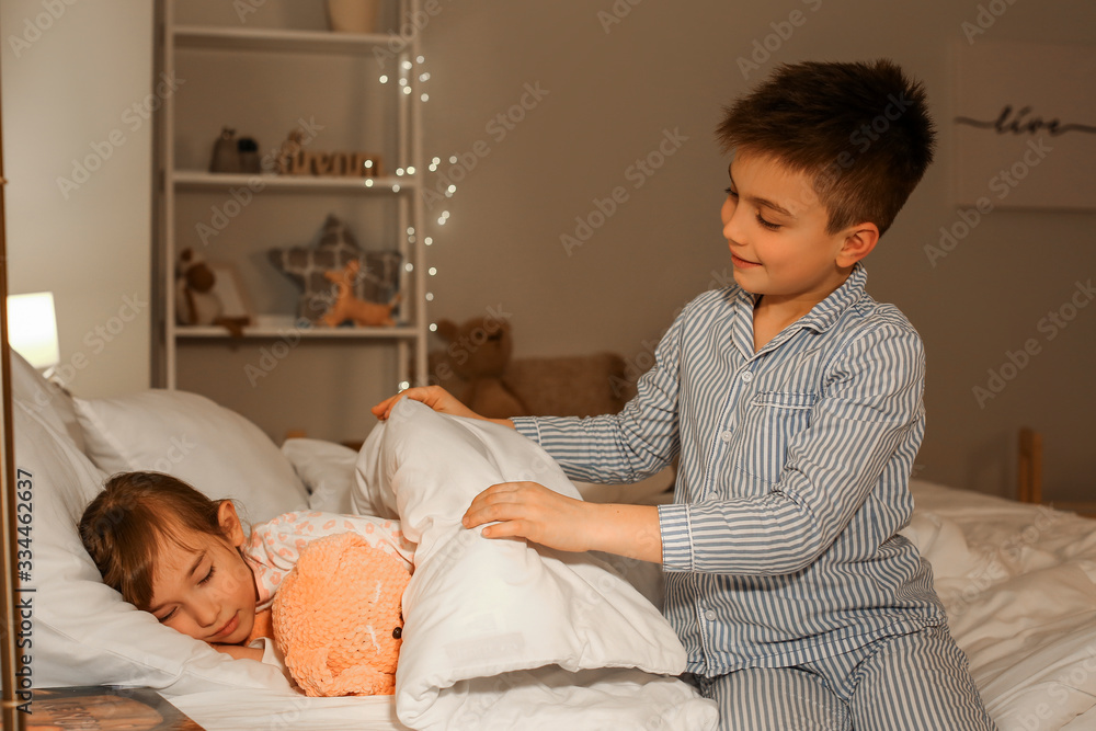 Little boy taking care of his sister in bedroom at night