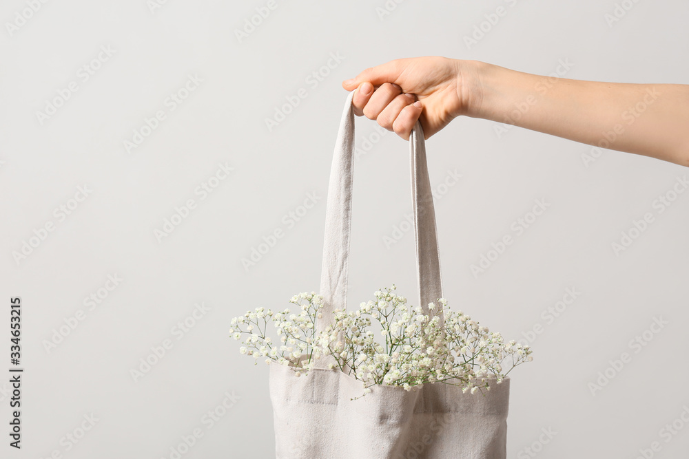 Female hand with flowers in eco bag on light background