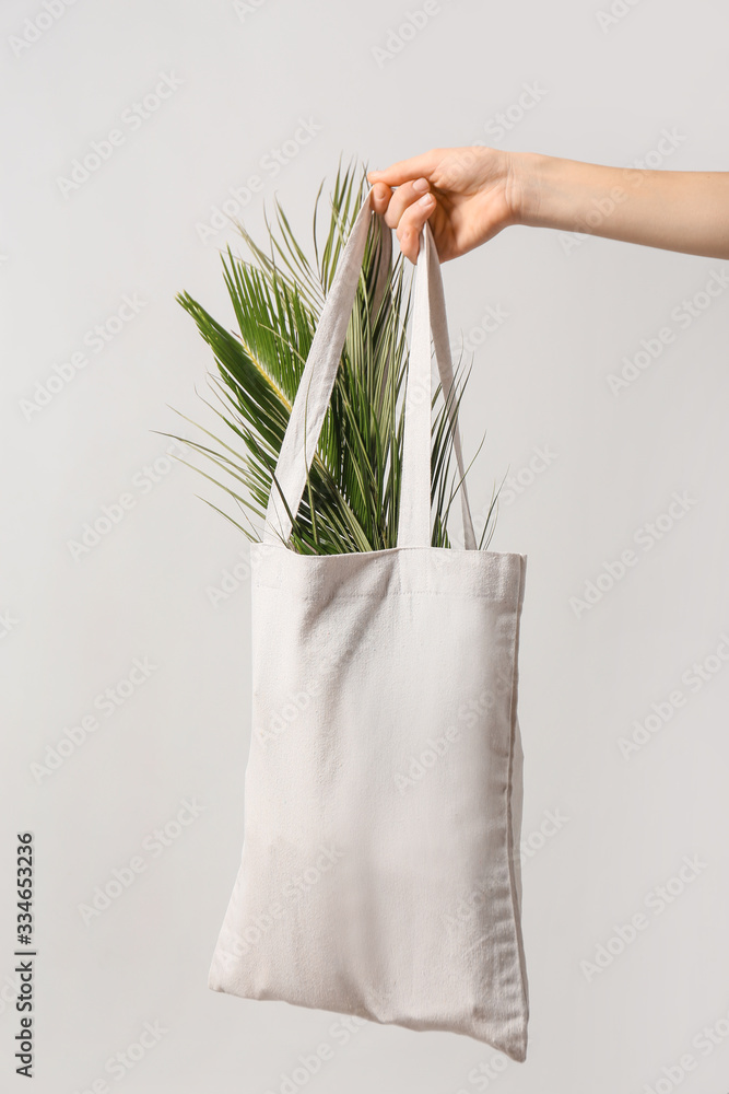 Female hand with eco bag on light background