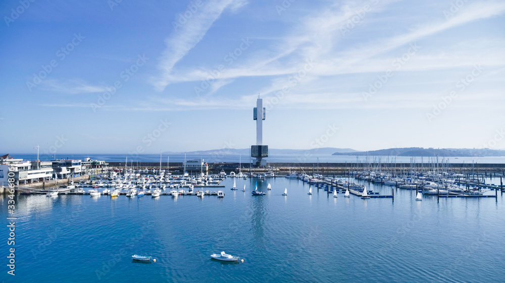 Sailboats docking at port and lighthouse gainst clear summer sky.