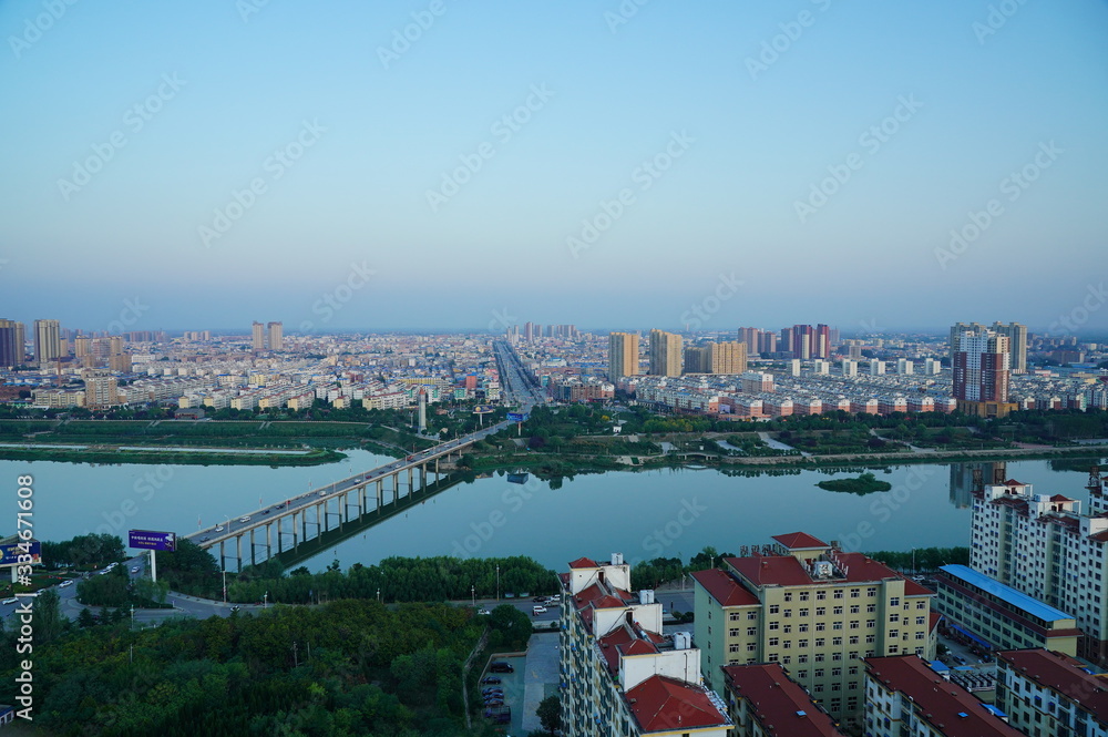 Aerial panoramic view of cityscape, houses under blue sky and bridge over river