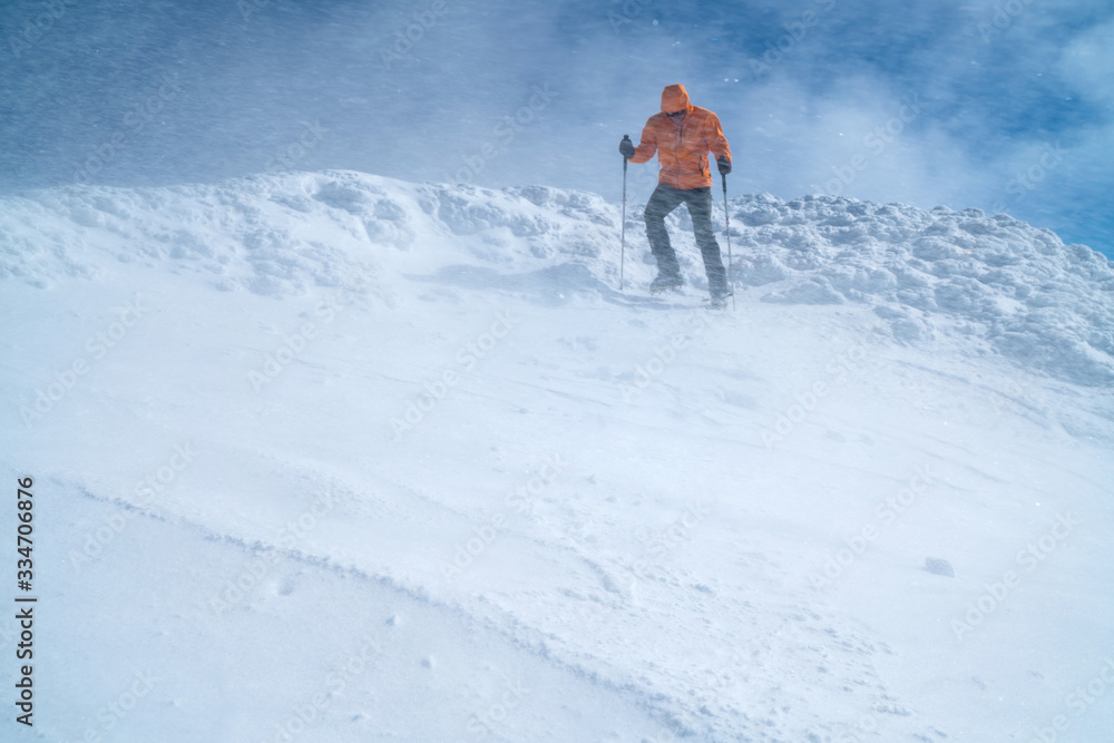 高山登山者穿着亮橙色软壳夹克，用登山杖从雪地上下来