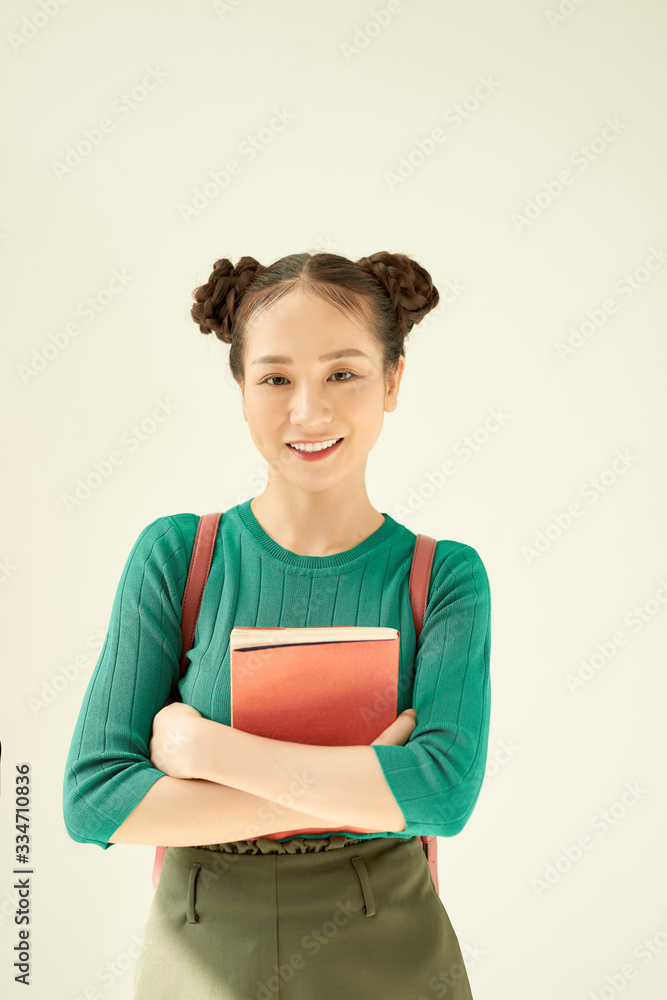 Portrait of a cheerful pretty asian girl holding books and looking at camera isolated over light bac