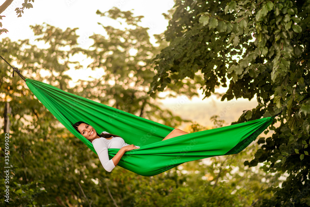 Portrait of a beautiful young woman lying on hammock in woods.