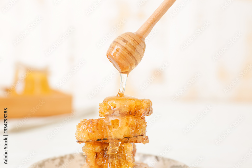 Honey dripping from dipper on tasty honeycombs on table