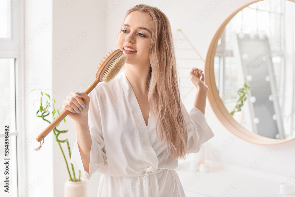 Beautiful young woman with brush in bathroom