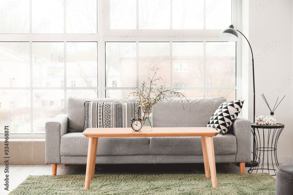 Interior of modern room with comfortable sofa, table and spring flowers