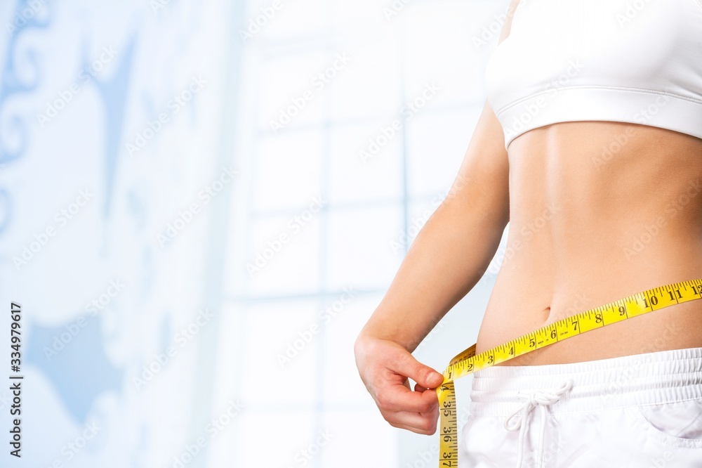 Slim young woman measuring thin waist with a tape measure