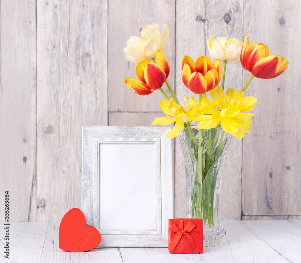 Tulip flower in glass vase with picture frame decor on wooden table background wall at home, close u