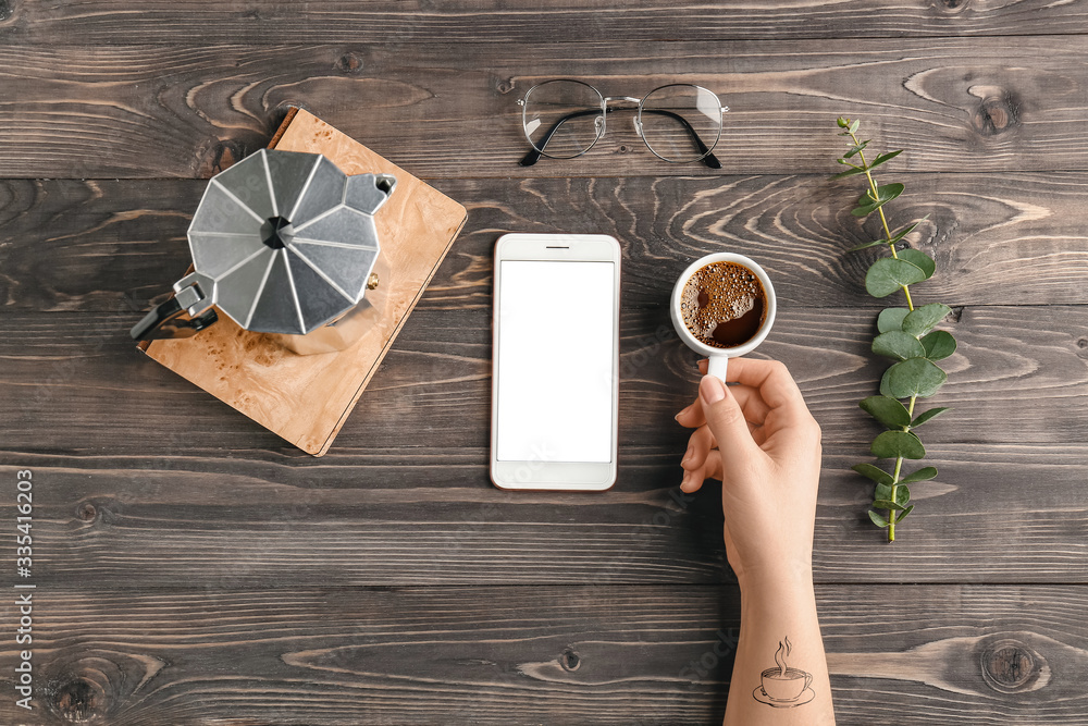 Female hand with cup of coffee and mobile phone on wooden background