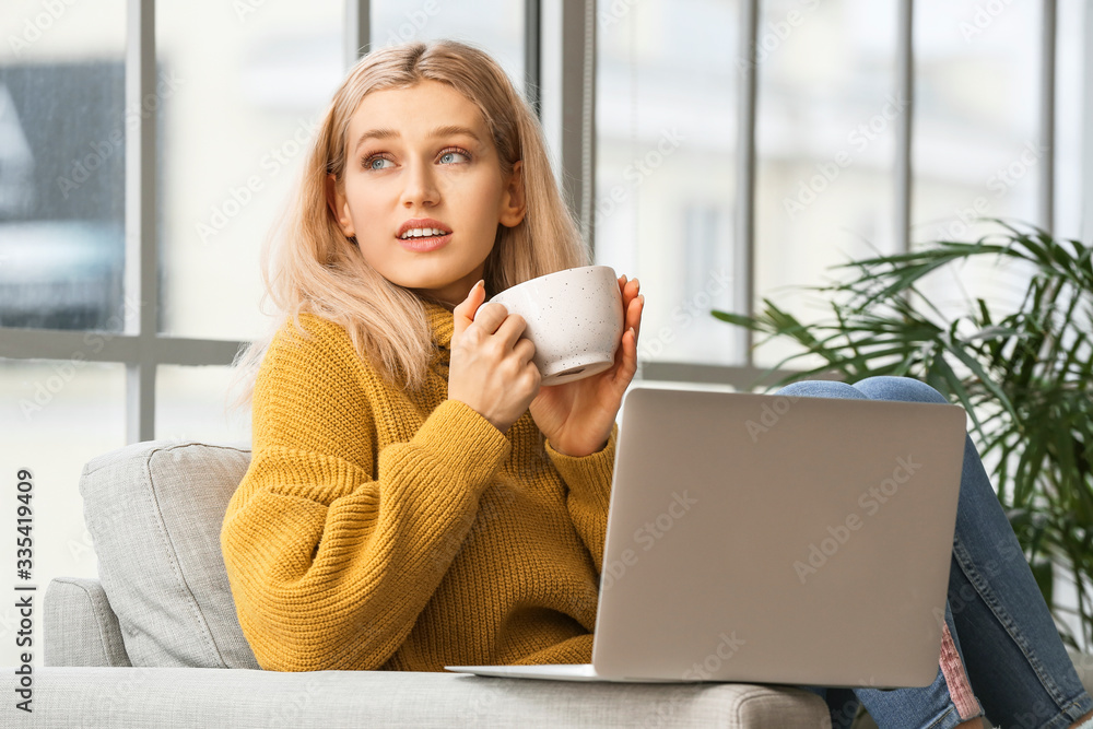 Beautiful young woman with laptop drinking tea at home