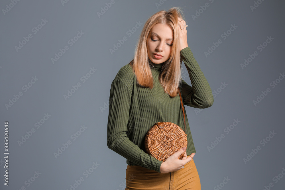 Young woman in warm sweater and with stylish bag on grey background