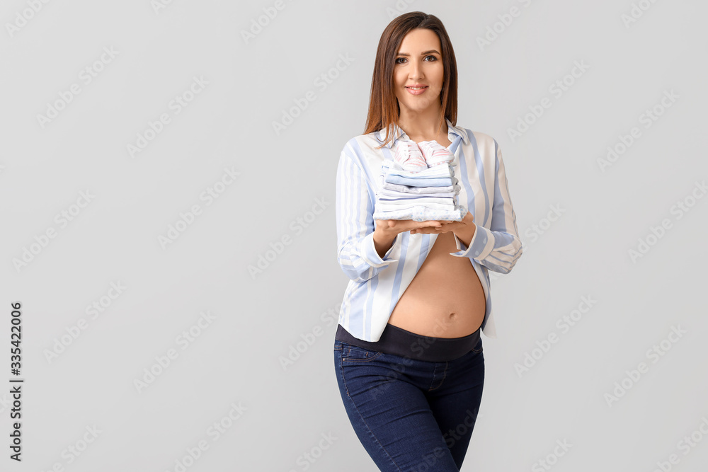 Beautiful pregnant woman with baby clothes on grey background