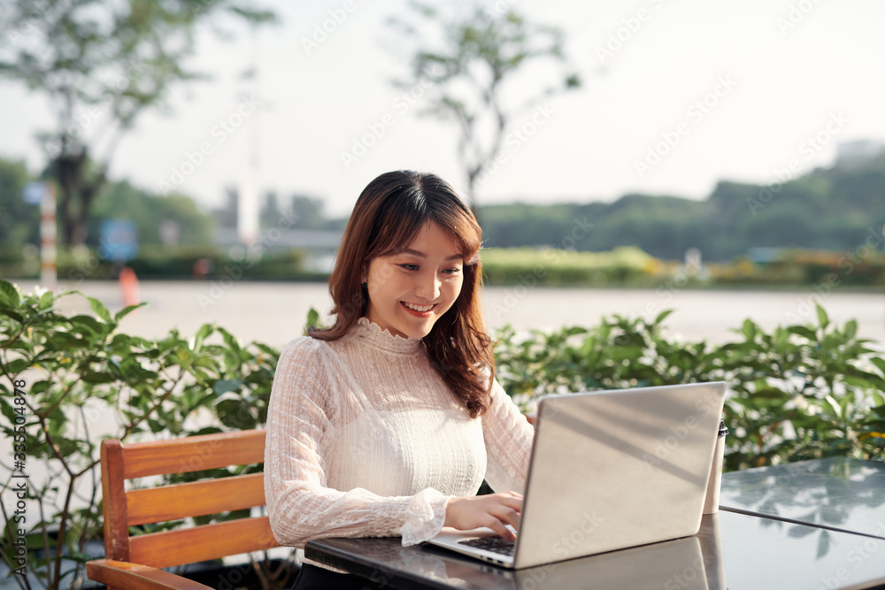 Happy casual beautiful woman using laptop sitting in a coffee shop outdoors in a sunny day