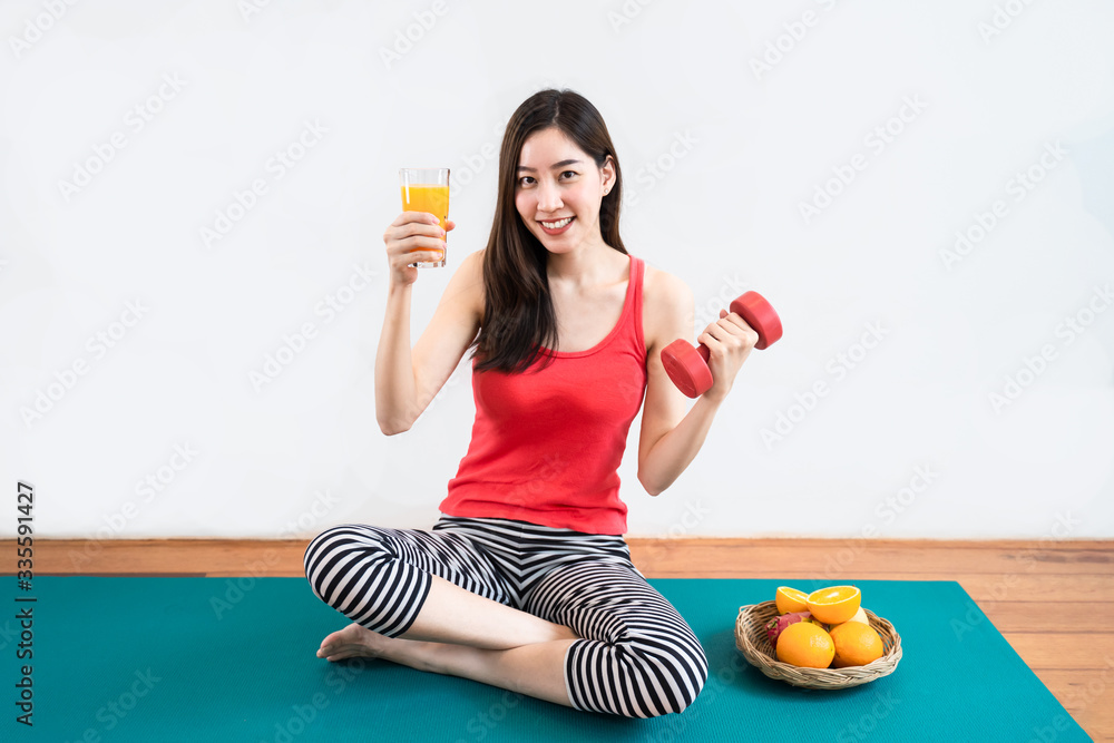 Asian young woman exercise and having fresh fruit and orange juice for healthy. Girl sit on yoga mat